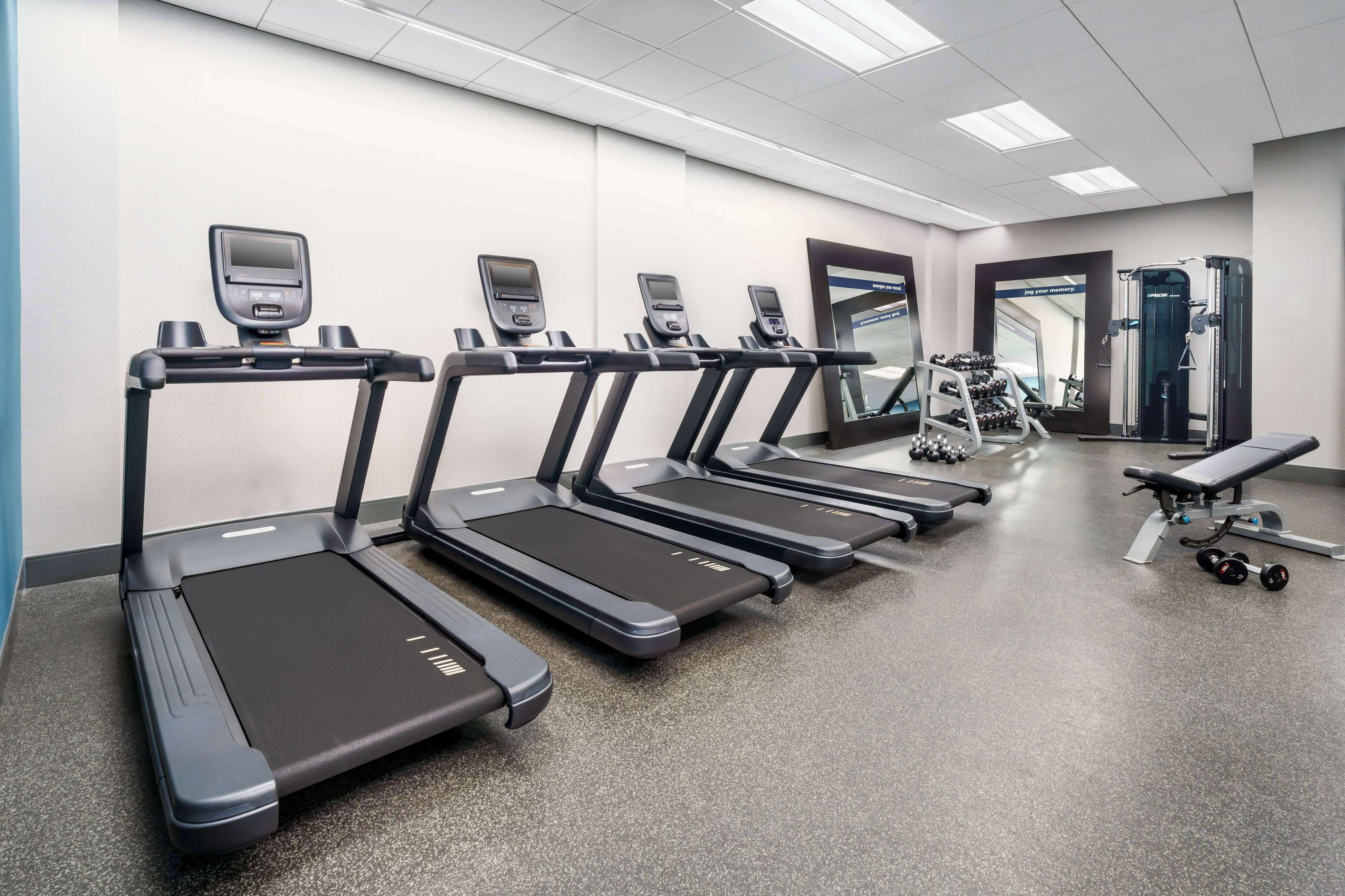 Un gimnasio con cintas de correr, pesas y una banca.