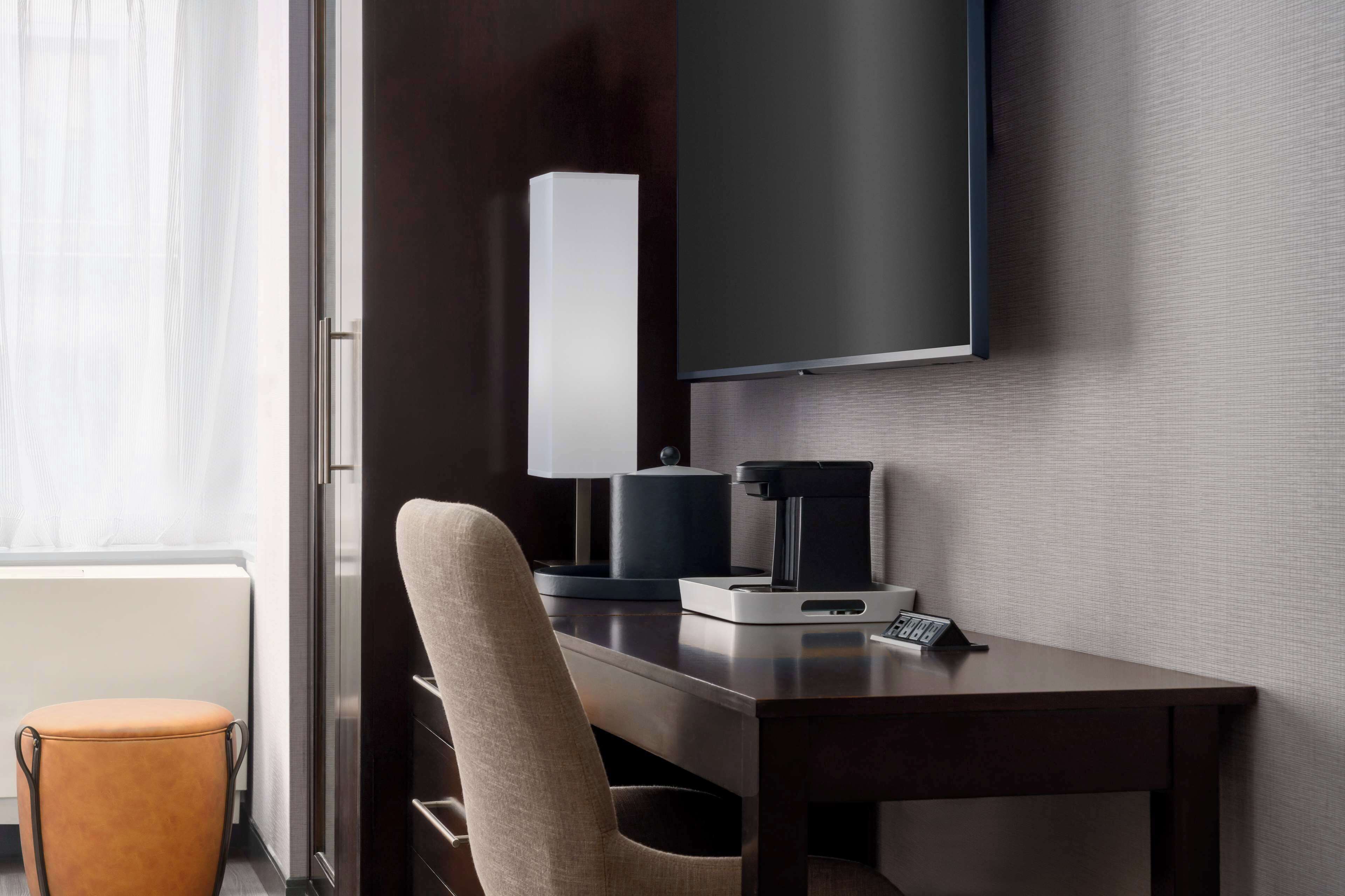Una habitación de hotel moderna con un televisor de pantalla plana montado en la pared, un escritorio con cafetera y una silla.