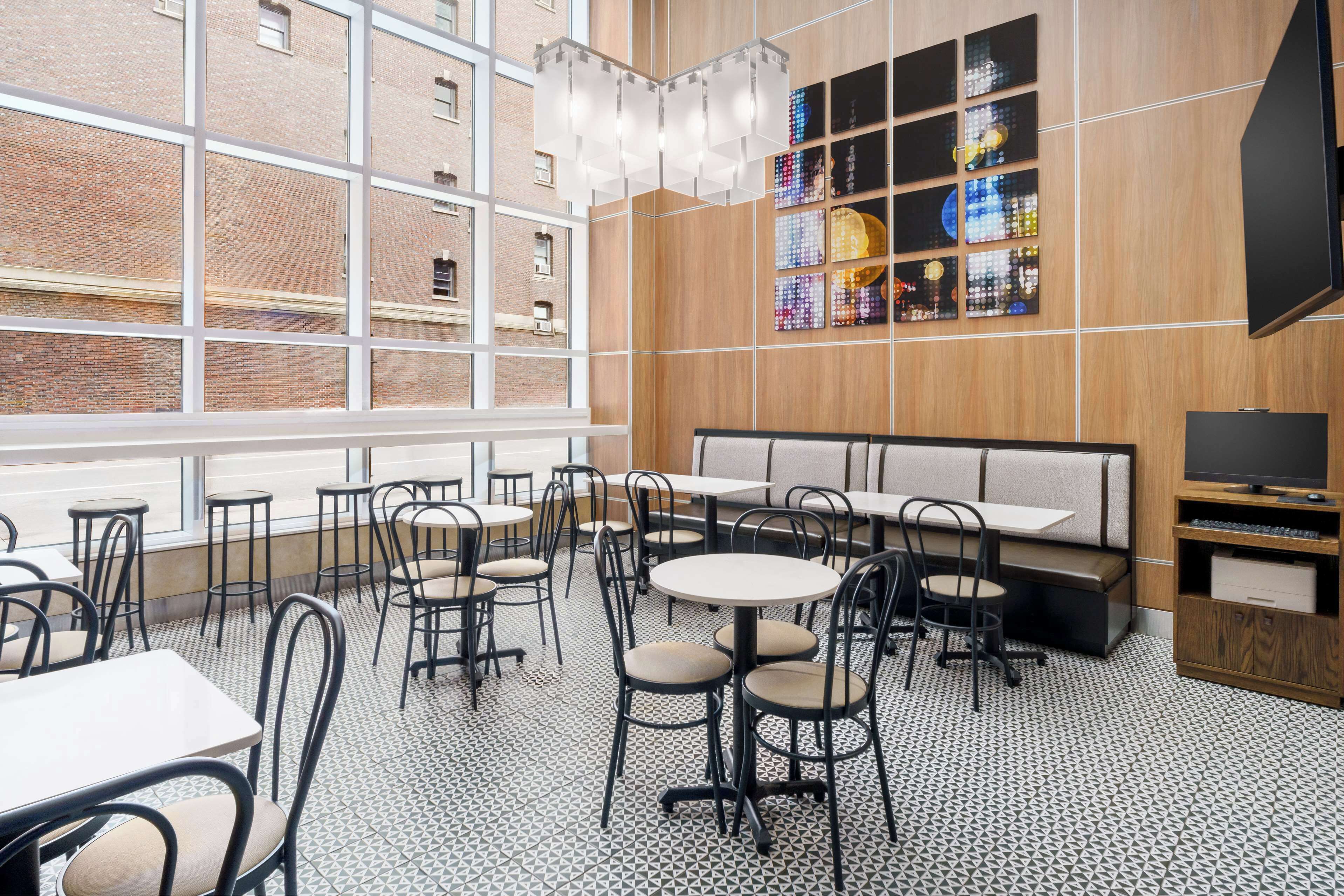 A modern restaurant with round tables and chairs, a large window, and a wooden wall with a stained glass art piece.