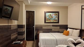 A hotel room with a bed, a TV, a painting, and a door.
