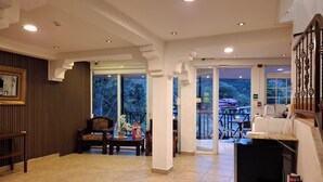 Un hall de hotel con un mostrador de recepción de madera, una zona de estar con una silla y una mesa, y vistas al exterior a través de amplios ventanales.