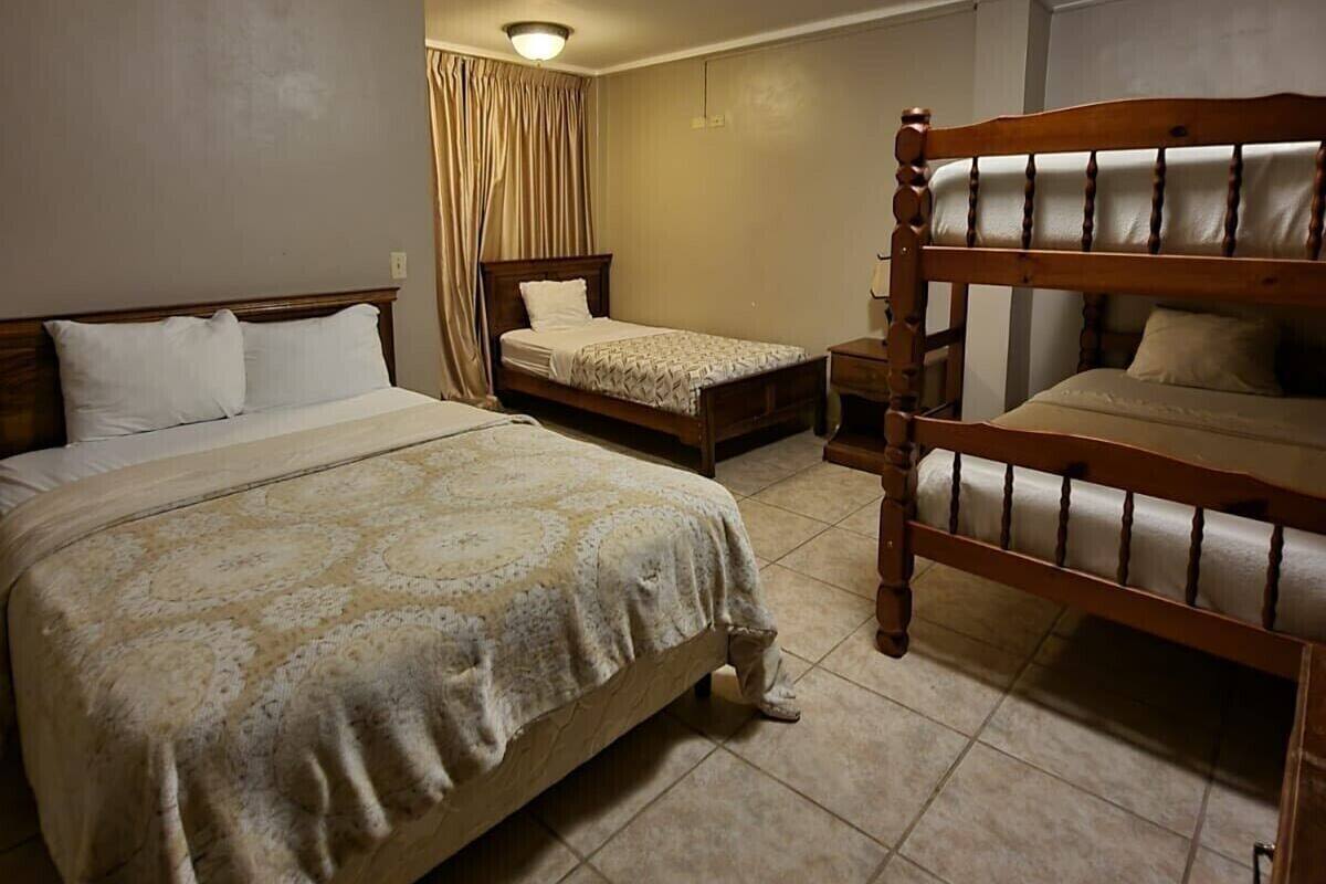 Une chambre d’hôtel avec un grand lit, un lit plus petit, un lit superposé et un luminaire au plafond.