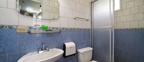 Baño con lavamanos, inodoro y zona de ducha blanca.