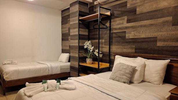 Habitación de hotel con dos camas, un revestimiento de madera en la pared, un estante con un jarrón de flores y una mesita de noche con artículos de aseo.