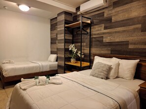 A hotel room with two beds, a wooden accent wall, a hanging shelf with a vase of flowers, and a bedside table with toiletries. - La Casa de la Abuela (Boquete)