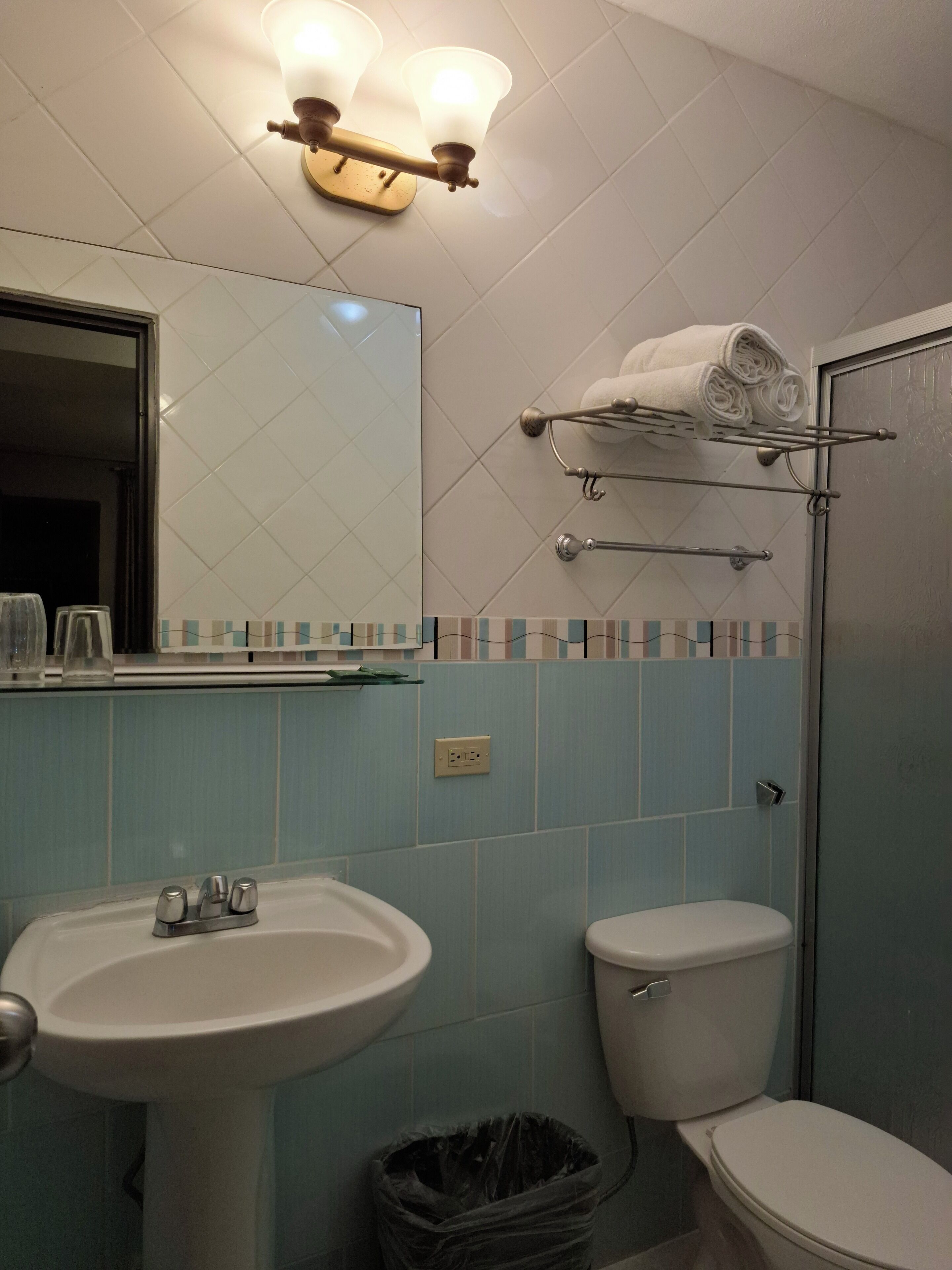 A bathroom with a sink, toilet, and a shower area. There is a towel rack with towels and a mirror above the sink.