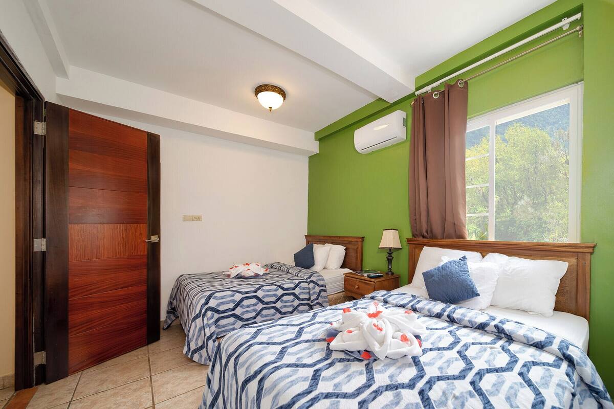 Une chambre d’hôtel avec deux lits, une fenêtre avec des rideaux, un appareil de climatisation et une porte en bois.