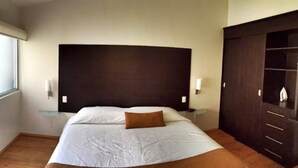 Een slaapkamer met een groot bed, een donker hoofdeinde, een glazen nachtkastje en een garderobe.