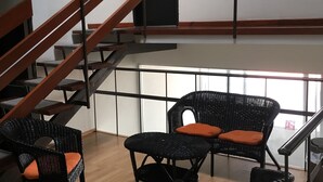 Een modern interieur met een trap, rieten meubels en een uitzicht door grote ramen.