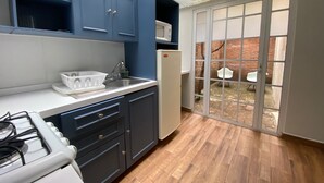 A kitchen with dark cabinets, a white countertop, a sink, and a stove. There is a glass door leading to an outdoor area with a brick wall and a white chair.
