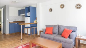 A compact living space with a kitchenette, a grey sofa with red cushions, and a wooden coffee table.