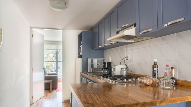 A modern kitchen with blue cabinets, a wooden countertop, and a view to a balcony.