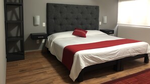 A modern bedroom with a tufted headboard, a wooden floor, a red and white bedspread, and a nightstand with a lamp.