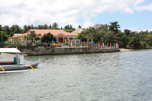 A waterfront property with a building featuring a red roof, a dock with a boat, and colorful flags.