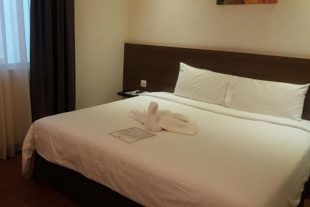 Cama bem arrumada com lençóis brancos, um travesseiro e uma toalha dobrada.