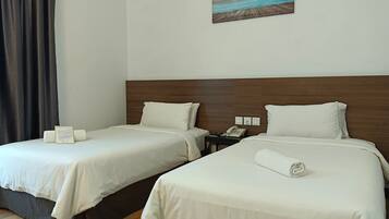 A hotel room with two beds, a wooden headboard, a painting of a beach, and a telephone on the nightstand.
