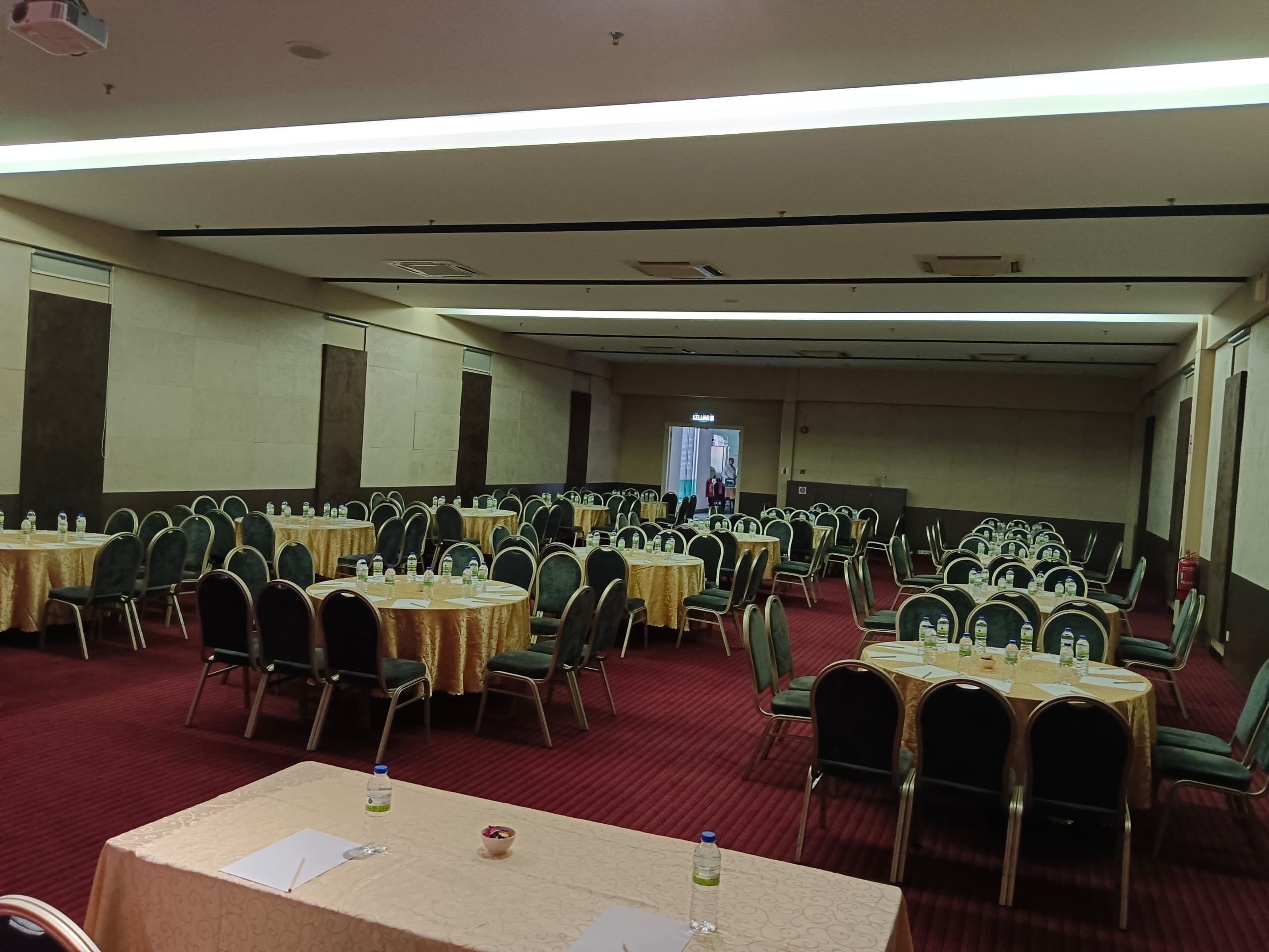 Un salón de conferencias con varias mesas y sillas dispuestas en filas, con botellas de agua y papeles sobre las mesas.