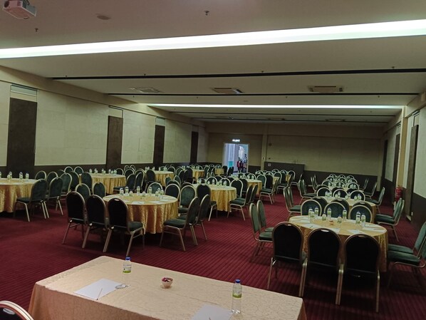 Un salón de conferencias con varias mesas y sillas dispuestas en filas, con botellas de agua y papeles sobre las mesas.