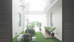 A narrow corridor with artificial grass, potted plants, and a view of a building in the distance. - Fuller Hotel (Alor Setar)