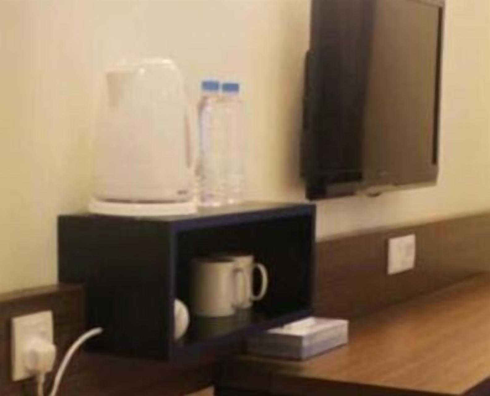 A hotel room with a coffee maker, a water bottle, and a TV mounted on the wall.
