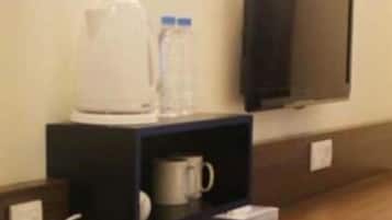 A hotel room with a coffee maker, a water bottle, and a TV mounted on the wall.
