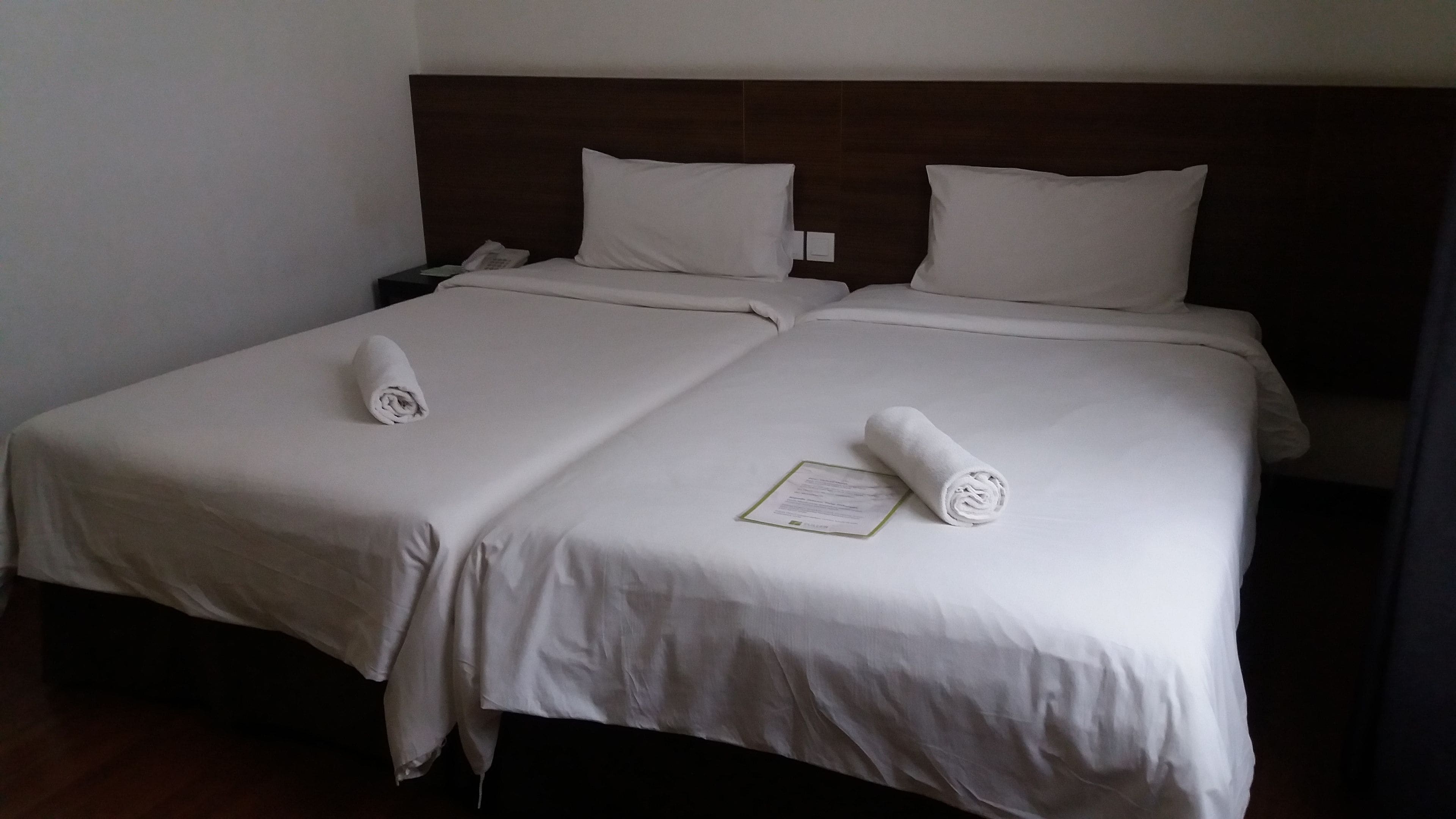 A double bed with white linens, two pillows, and a folded towel on each side.