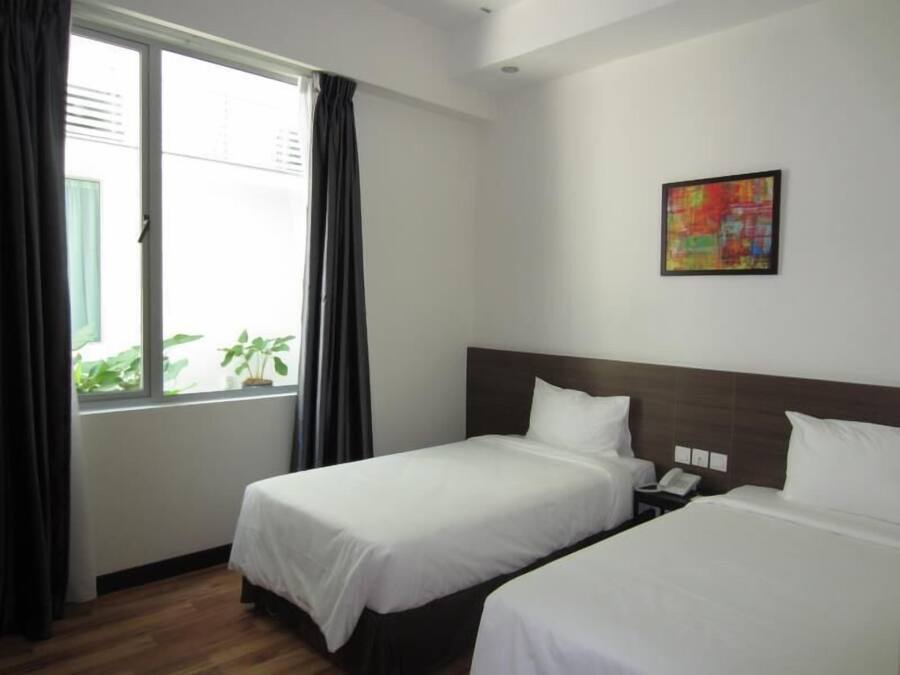 A hotel room with two beds, a window with curtains, a painting on the wall, and a small plant on the windowsill.