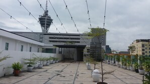 A building with a central tower, potted plants, and a paved area. - Fuller Hotel (Alor Setar)