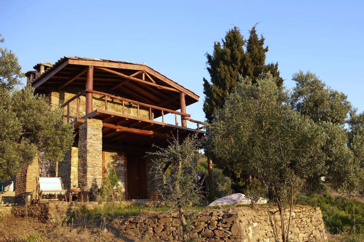 Un edificio de piedra rústico con un balcón de madera, rodeado de olivos y una pared de piedra.