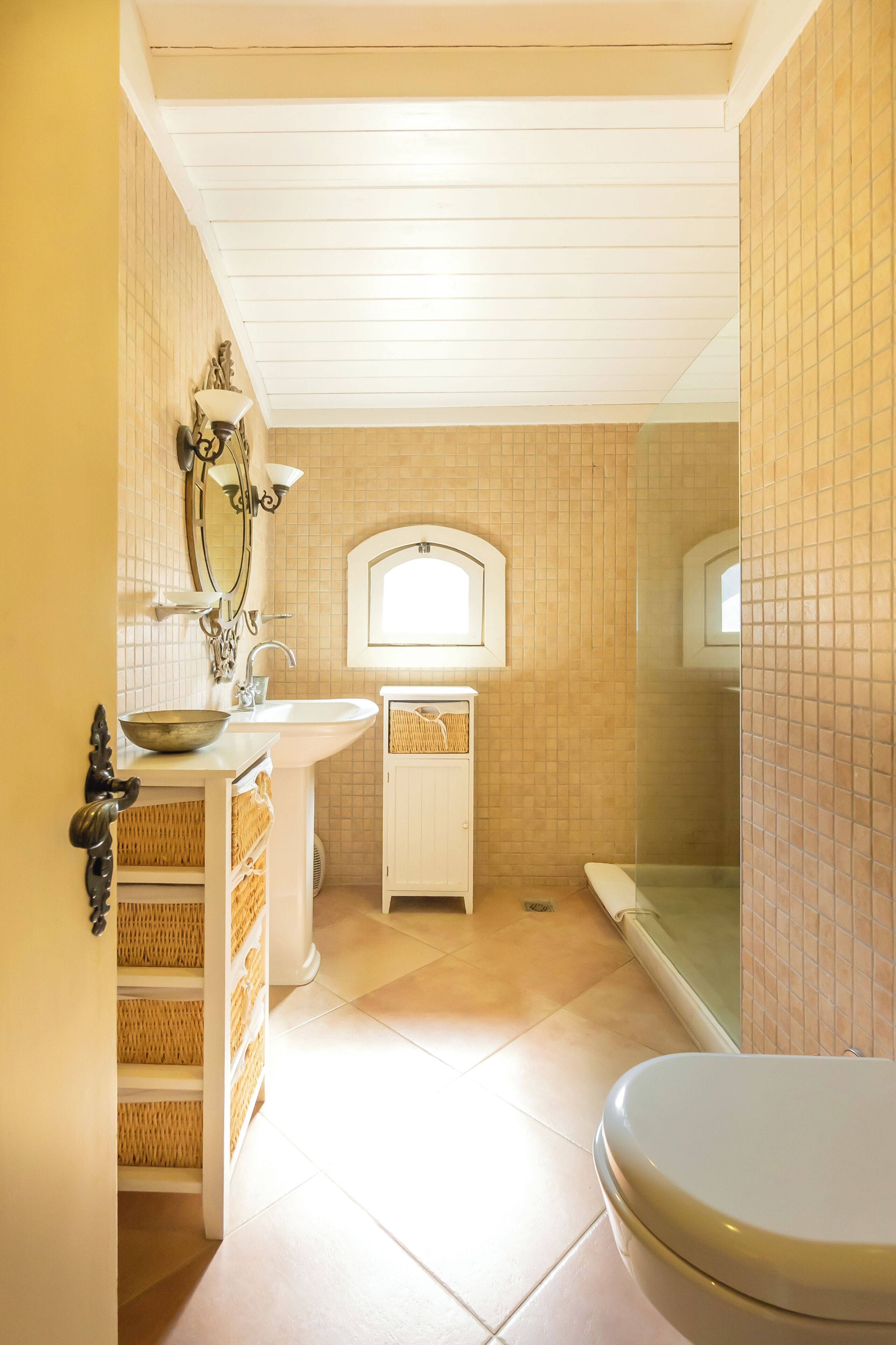 A bathroom with a white sink, a mirror, a window, and a shower area.