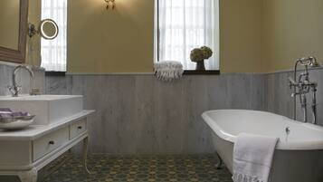Un baño con una bañera independiente, un tocador con espejo y un espejo redondo, una ventana con cortinas y un suelo estampado.
