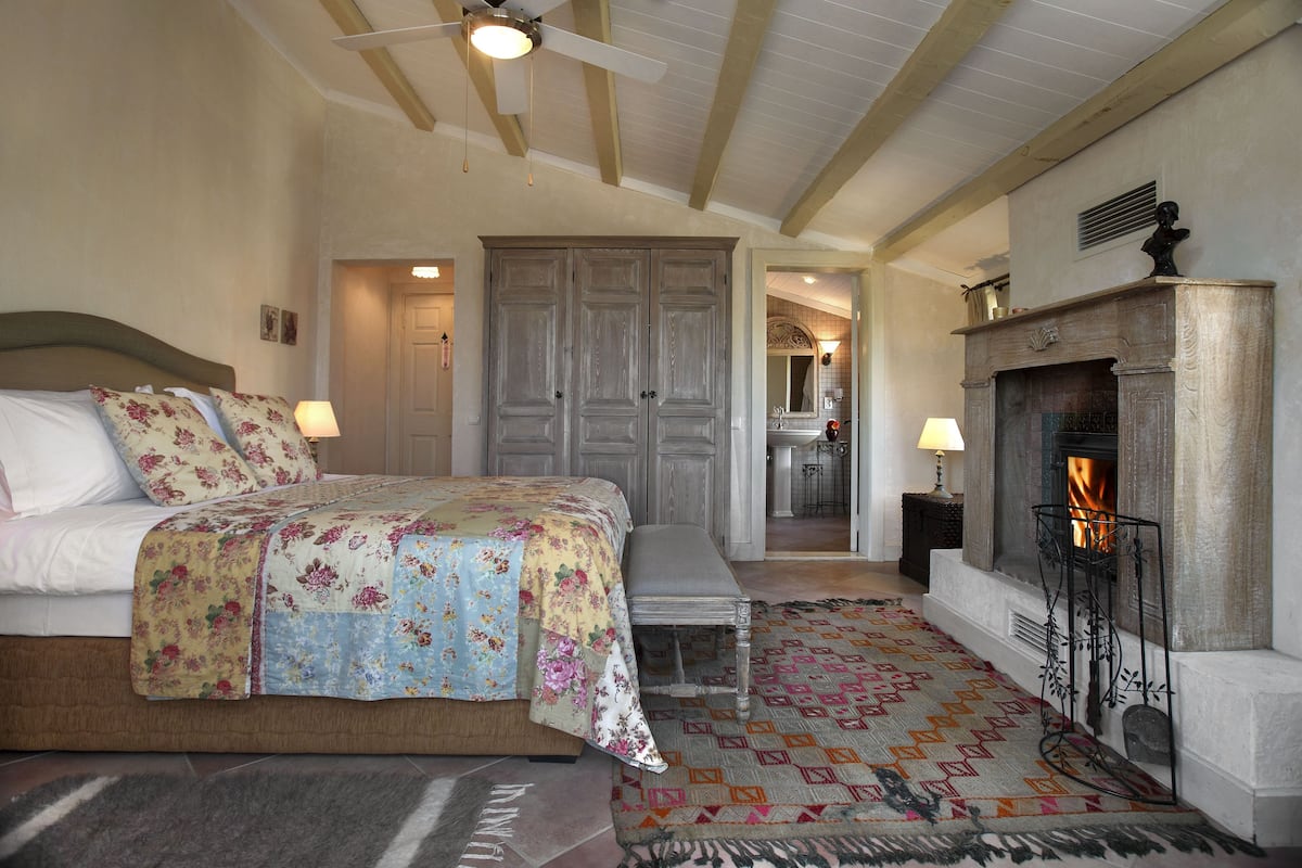 Un dormitorio con cama, banco, chimenea y una puerta que da a un baño.