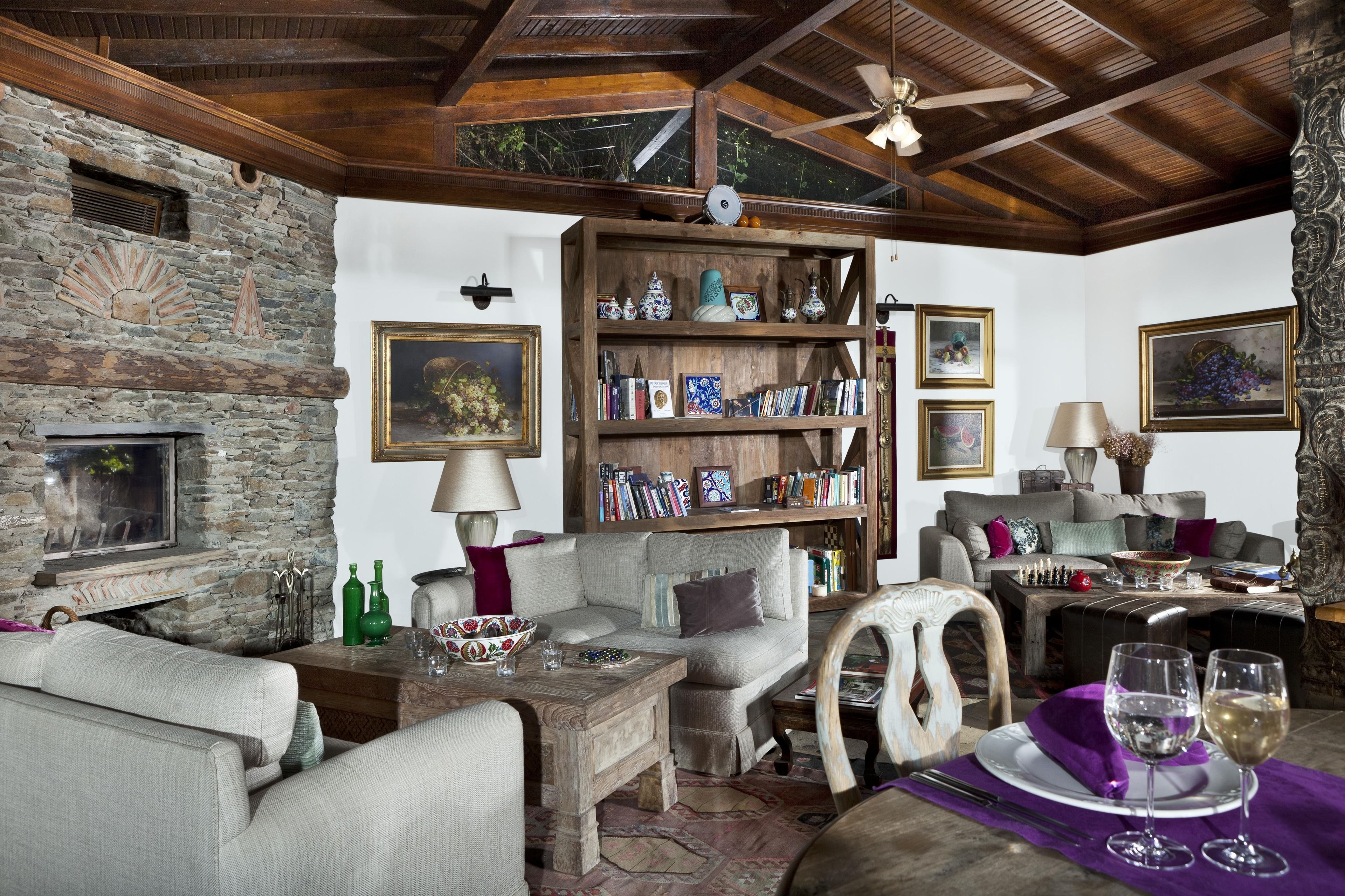 A cozy living room with a stone wall, wooden ceiling, and a bookshelf filled with books and decorative items.