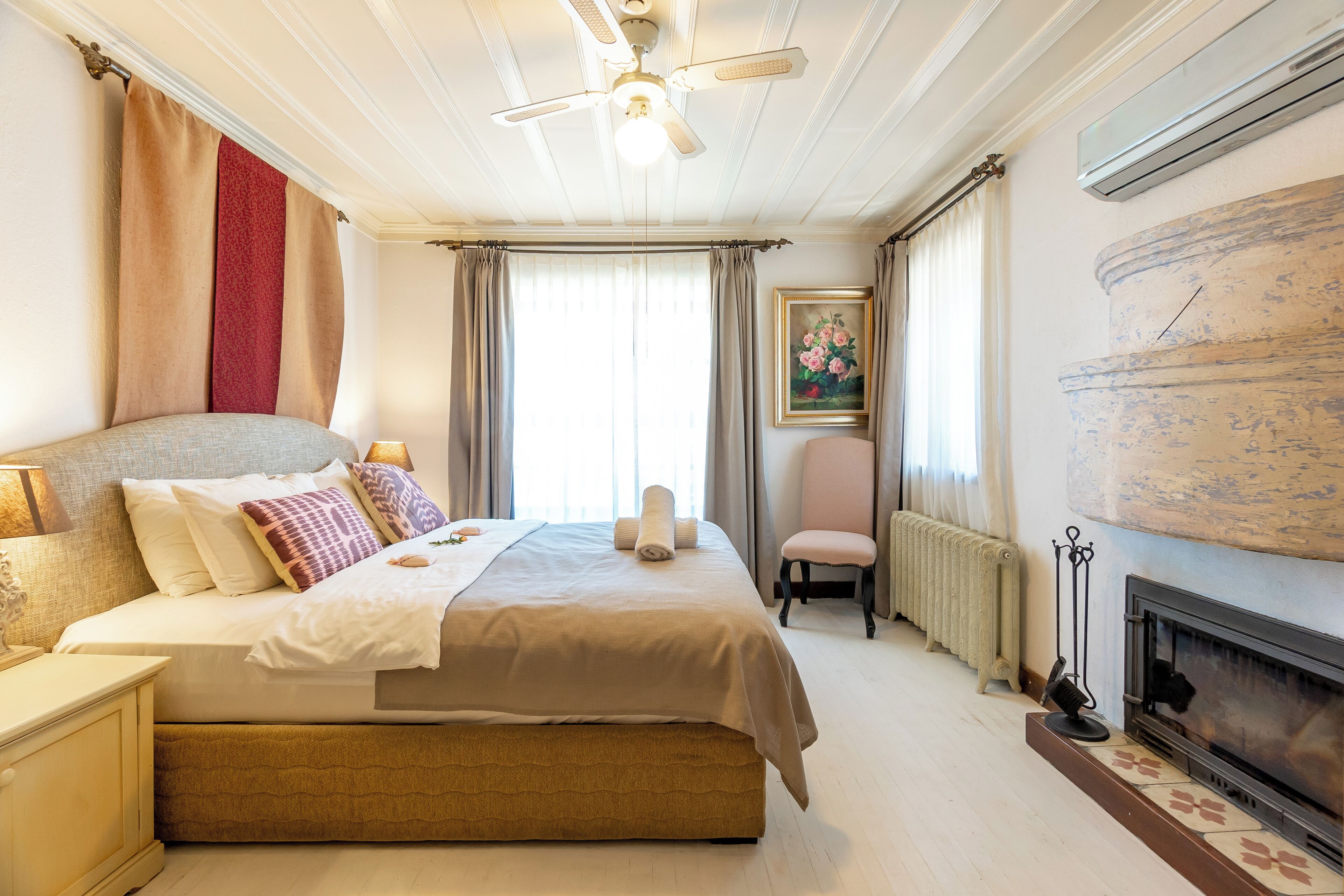 Une chambre d’hôtel avec un lit, une chaise, une cheminée et une fenêtre avec des rideaux.