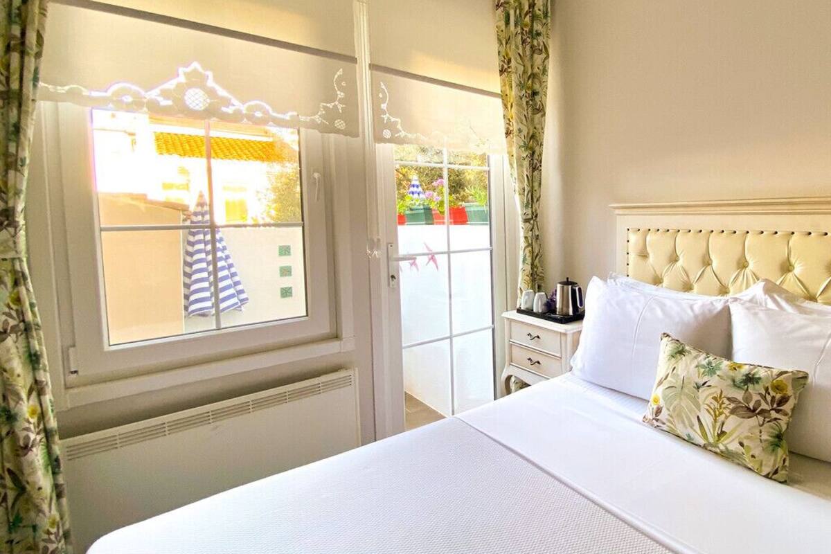 A hotel room with a large bed, a bedside table, a window with curtains, and a view of the outside.