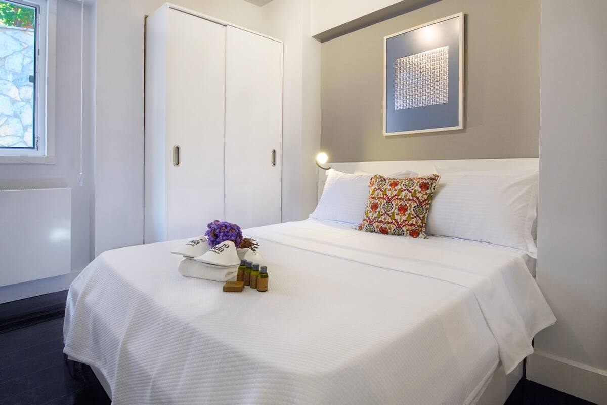 A neatly made bed with a white comforter, a floral pillow, and a pair of white sneakers on the bed.