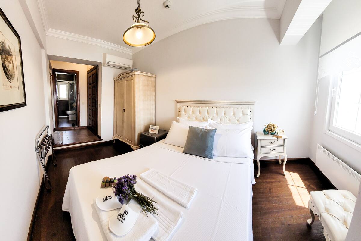 A hotel room with a large bed, a bedside table, a nightstand, a wardrobe, and a bathroom visible through an open door.