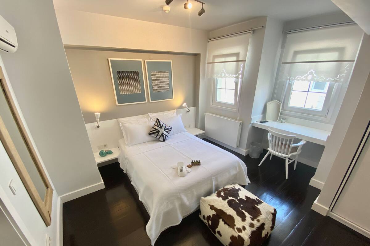 A bedroom with a bed, a desk, a chair, a radiator, and artwork on the wall.