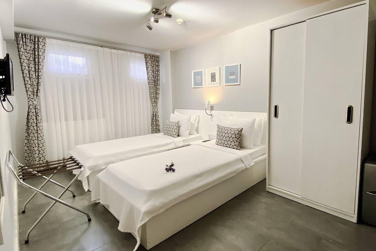 A hotel room with two beds, a wardrobe, a desk, and a window with curtains.