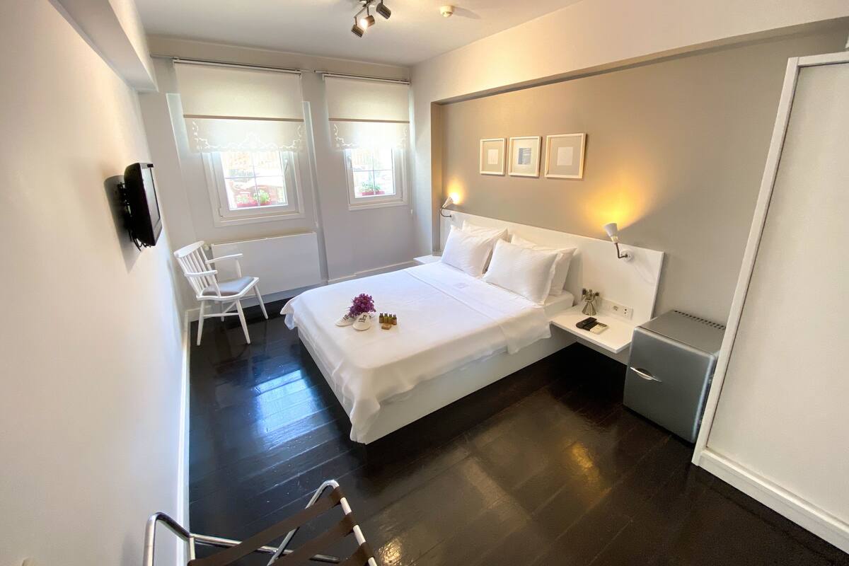 A modern hotel room with a large bed, a bedside table, a chair, and a desk.