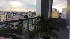A balcony with a view of a cityscape, including buildings and a palm tree. - Hau Giang 2 (Can Tho)
