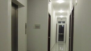 A long, narrow hallway with a shiny tiled floor, doors on both sides, and a staircase leading to an elevator. - Hau Giang 2 (Can Tho)