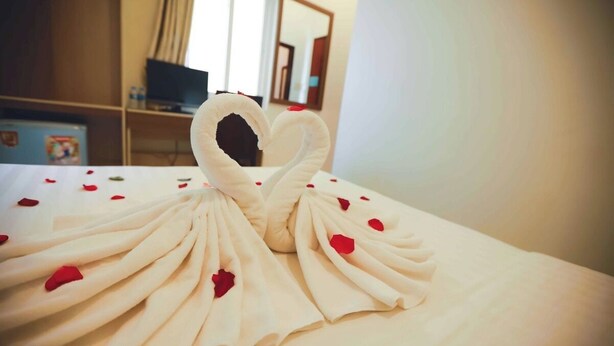 A bed with a swan-shaped towel arrangement and red rose petals. - Hau Giang 2 (Can Tho)