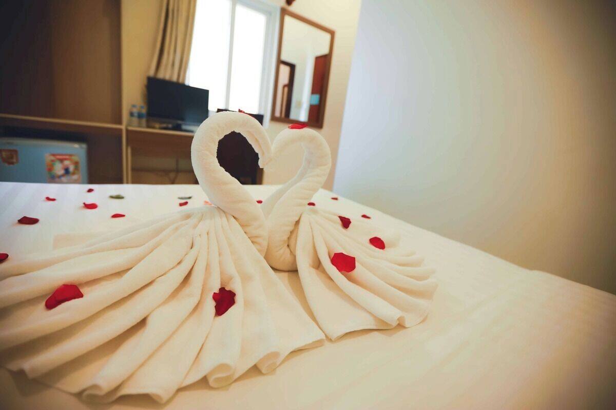 Una cama con un arreglo de toallas en forma de cisne y pétalos de rosa roja.