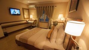 Une chambre d’hôtel comprenant un lit, une table de chevet, une lampe, un bureau, une chaise, une télévision et des rideaux.
