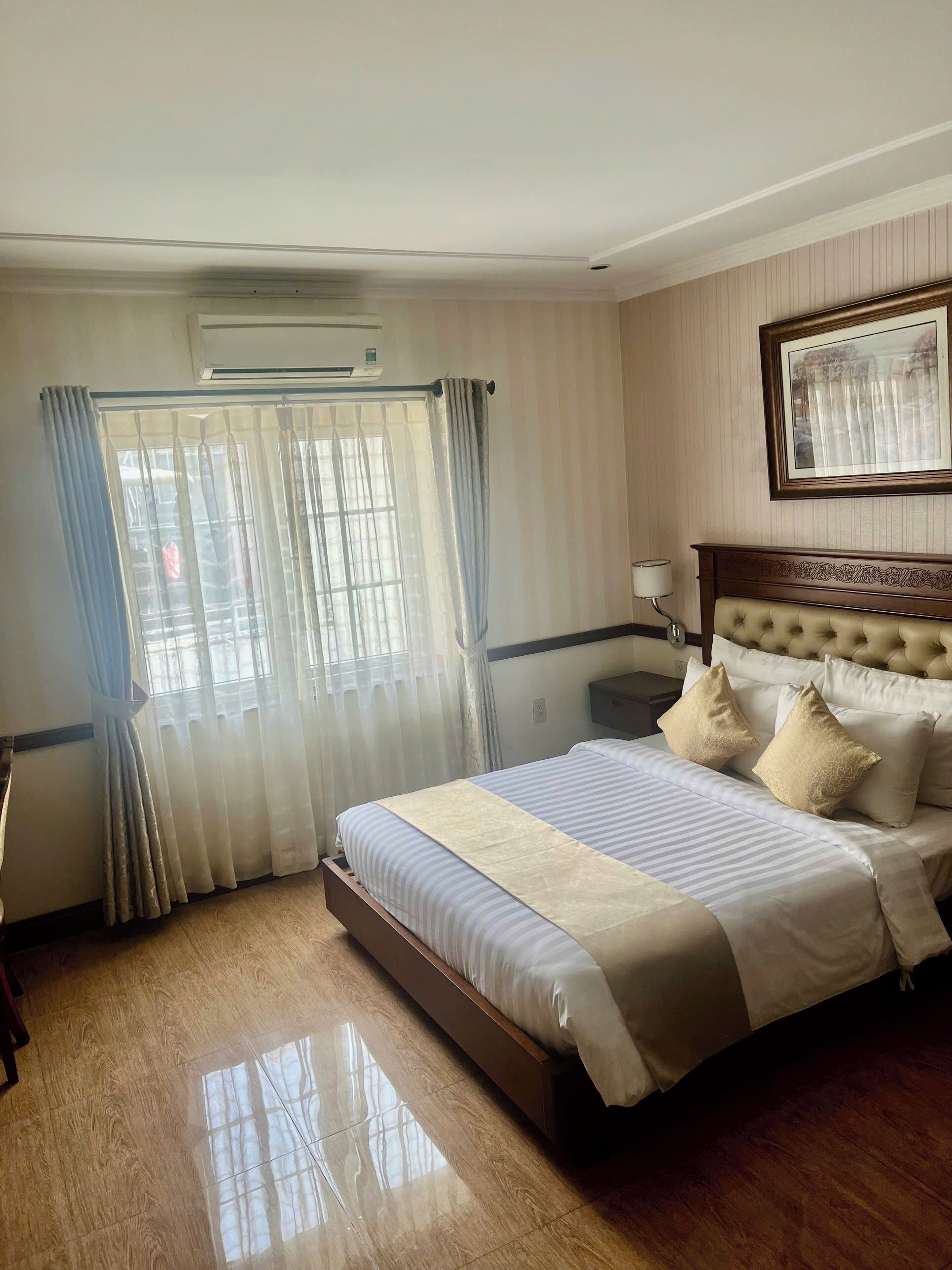 A hotel room with a large bed, a bedside table, a lamp, and a window with curtains.