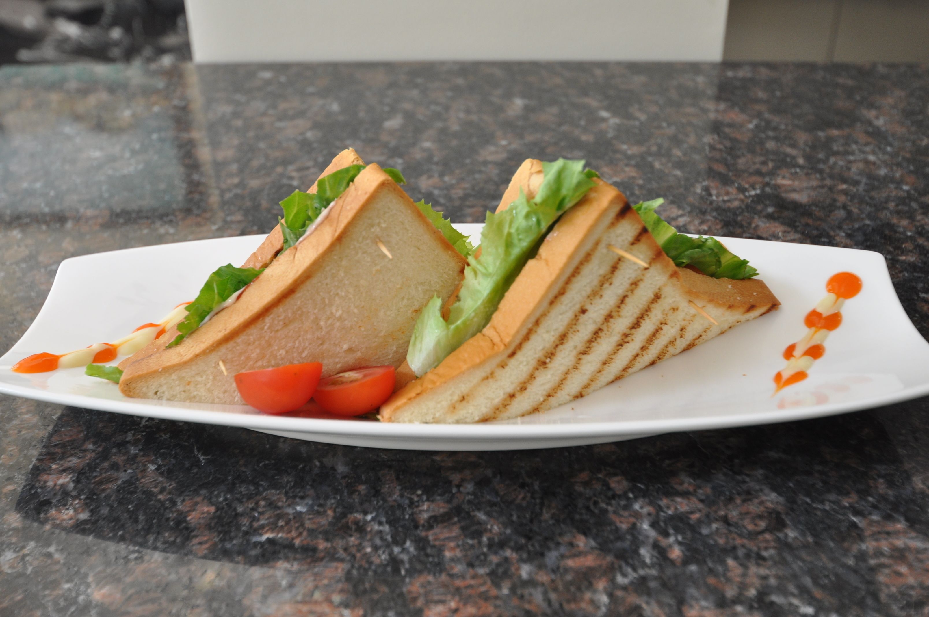 A sandwich on a white plate with a tomato and some sauce.