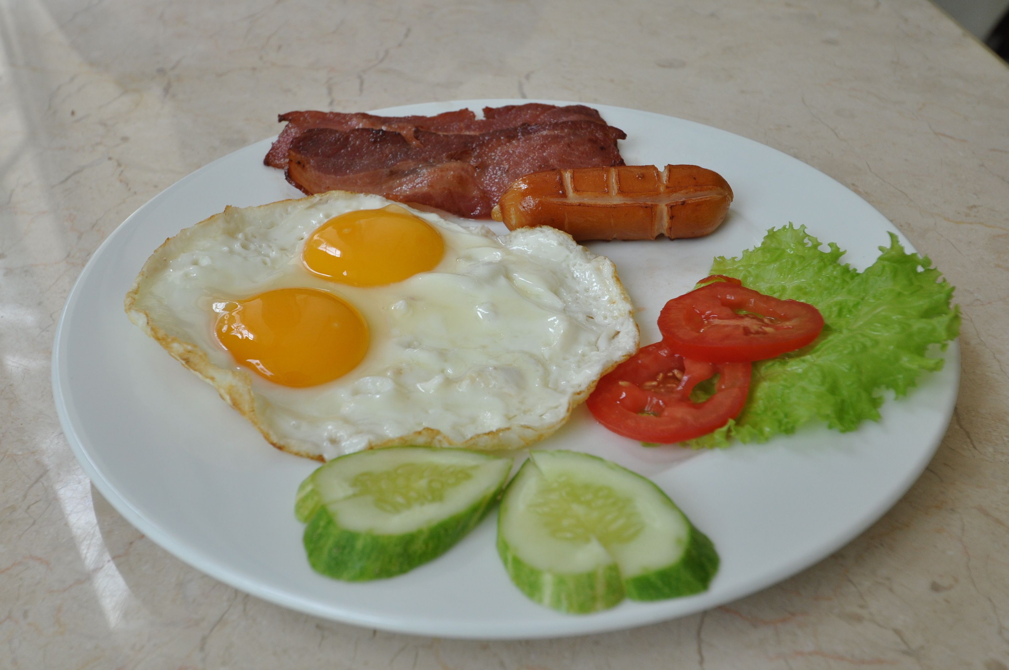 Une assiette avec des œufs, du bacon, des saucisses, de la laitue et des tomates.