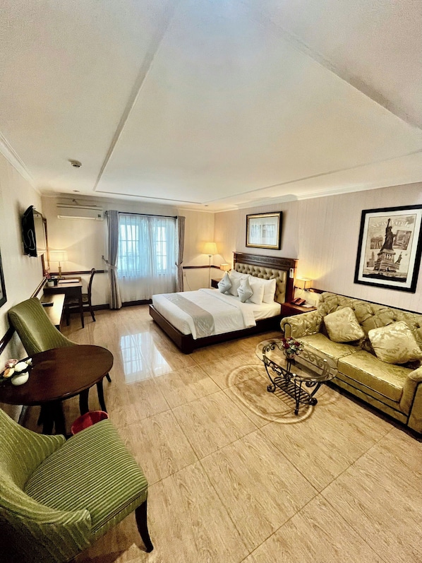 Una habitación de hotel con una cama, un sillón verde, un sofá, una mesa de comedor y una mesa de centro.