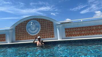 Una piscina con agua azul cristalina, una persona en la piscina y un edificio con fachada decorada al fondo.